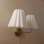 Double-head wall lamp with two pleated white shades, gold bracket, cord hanging
