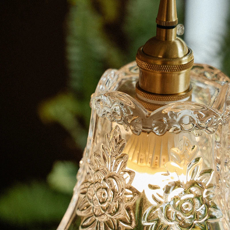 Close-up of clear floral pressed glass shade on brass wall sconce with glowing bulb