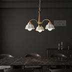 Scandinavian-style chandelier with gold arms, brown column, and five white scalloped shades.