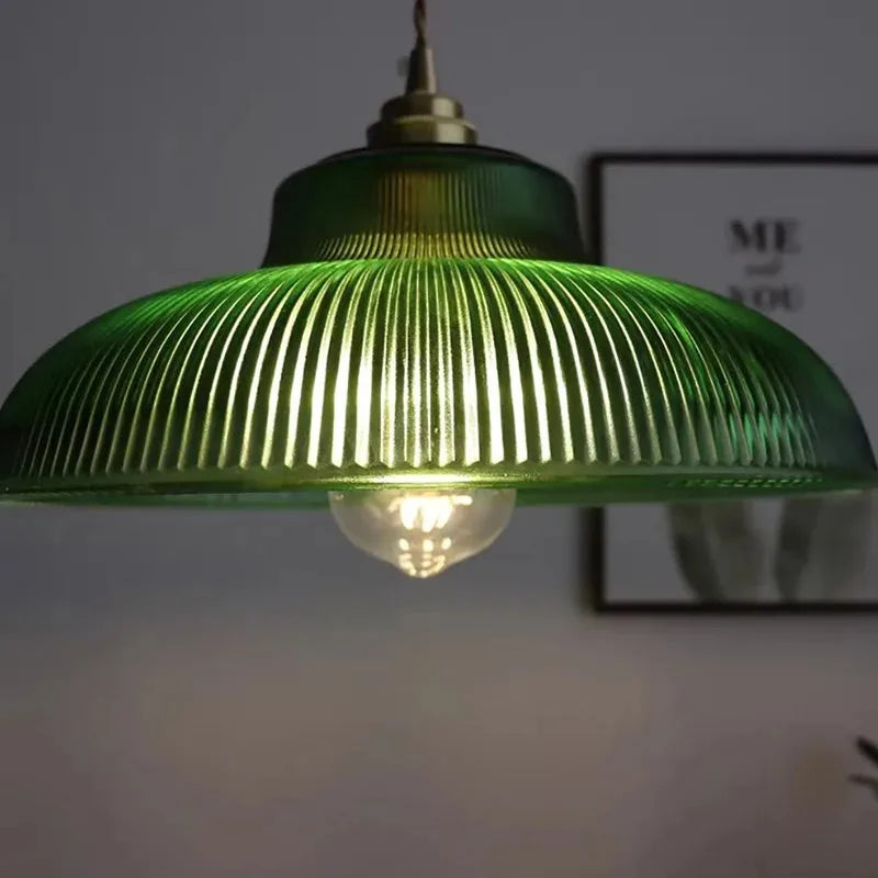 Green ribbed glass dome pendant light glowing with brass top and hanging cord