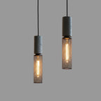 Pair of tubular cage pendant lights with dark speckled cylinders and warm glowing filament bulbs