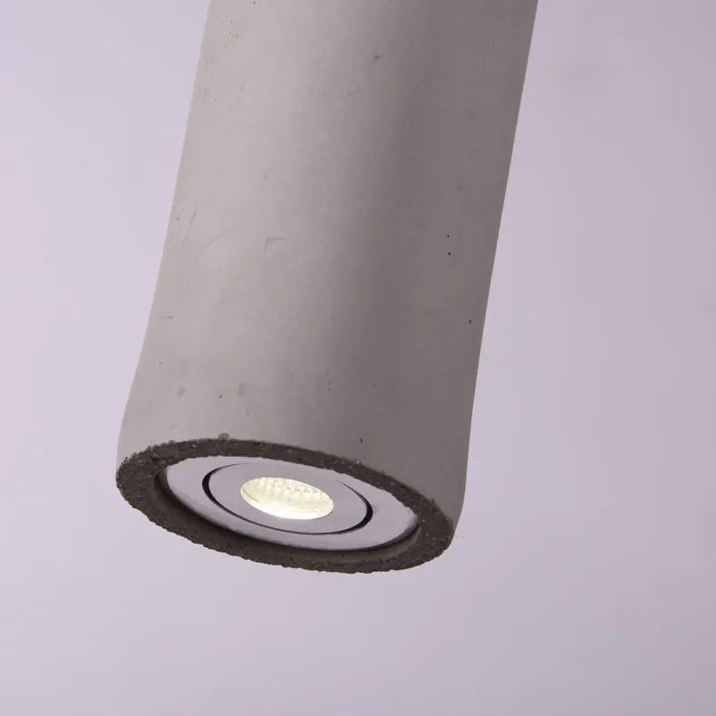 Tubular pendant light with speckled gray concrete housing and recessed glowing bulb