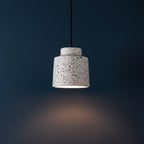 Stepped drum pendant light with speckled white shade and black cord, glowing
