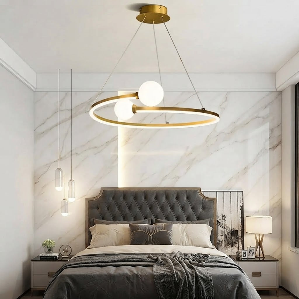 Gold ring LED chandelier with three white globe lights above a bed in a marble room