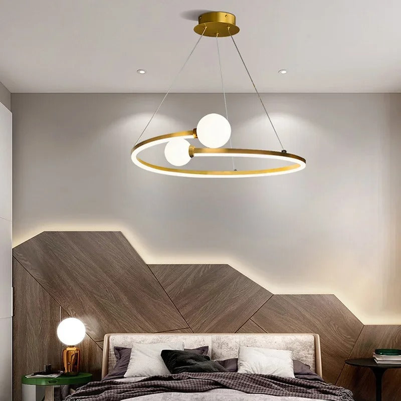 Gold ring halo LED chandelier with three white globe lights hanging above a bed
