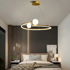 Gold ring LED chandelier with three white globe lights hanging over a bedroom bed