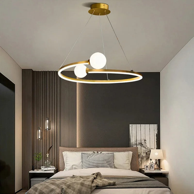 Gold ring LED chandelier with three white globe lights hanging over a bedroom bed