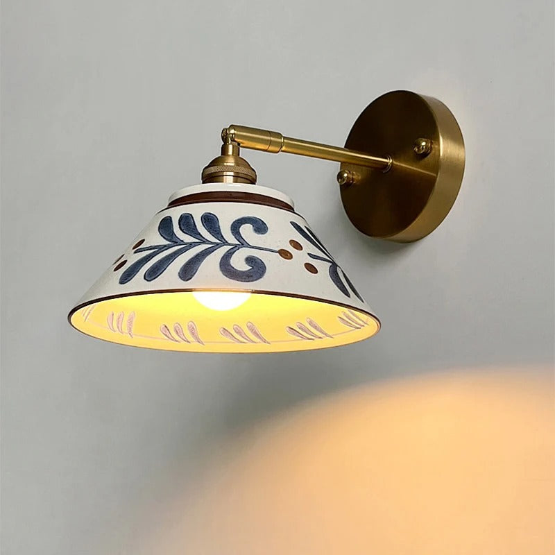 Brass wall lamp with ceramic shade showing blue leaf pattern and warm yellow glow
