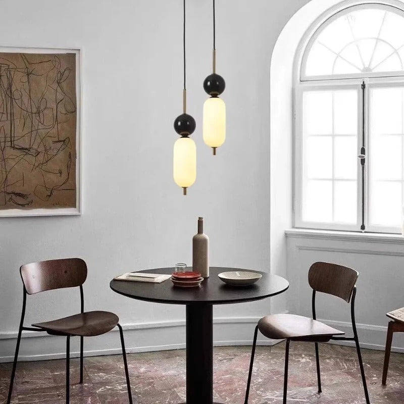 Two stacked glass cylinder pendant lights with black round tops and opal shades