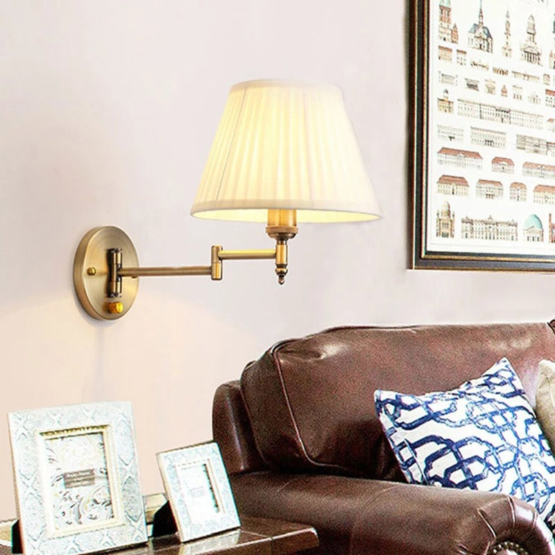 Brass wall sconce with fabric drum shade and swing arm on round backplate
