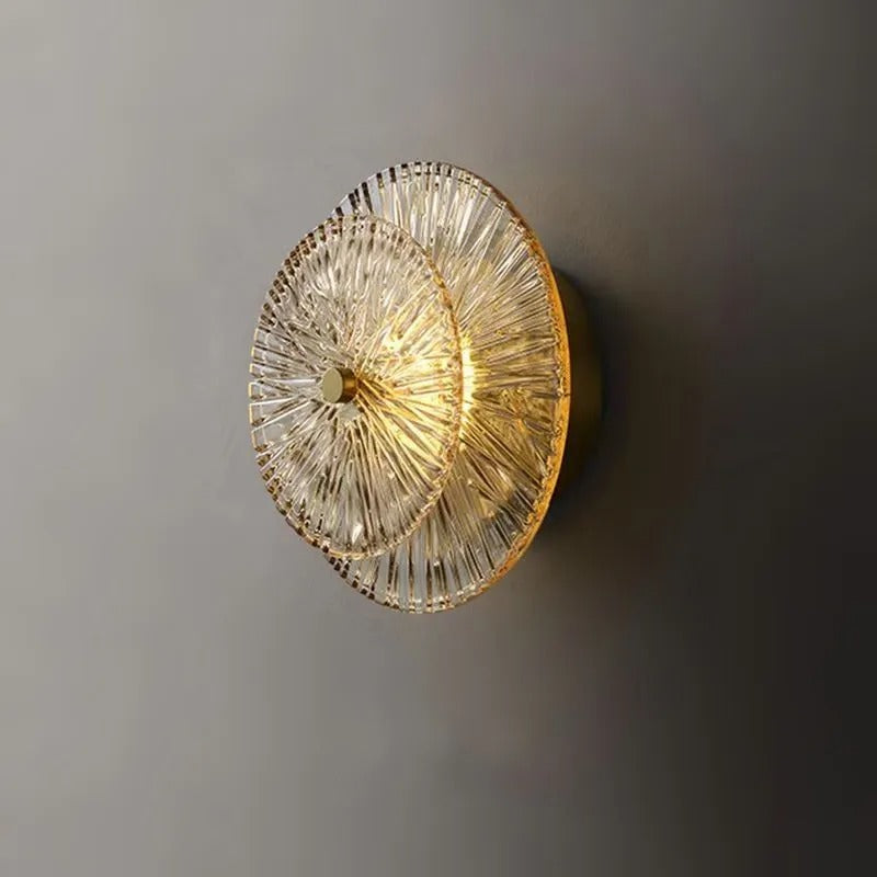 Circular tiered glass wall light with warm light glowing through clear glass rods