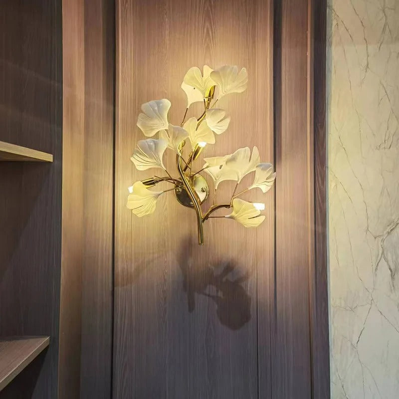 Gold ginkgo-style wall sconce with glowing off-white leaf shades on wooden panel