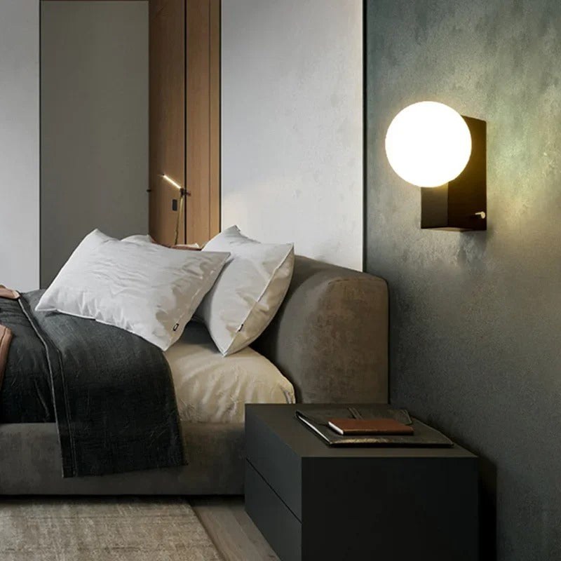 Spherical globe wall light with black mount and frosted white globe, emitting warm light
