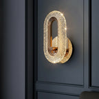 Gold textured oval wall sconce with brass details mounted on a dark panel