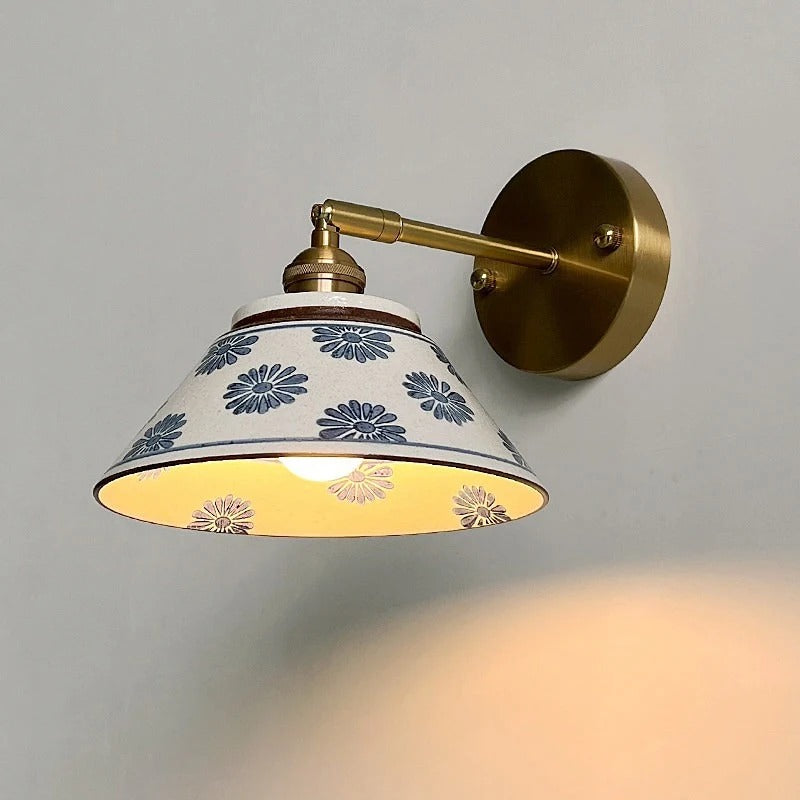 Brass wall light with round backplate and ceramic shade with blue daisy-like flowers