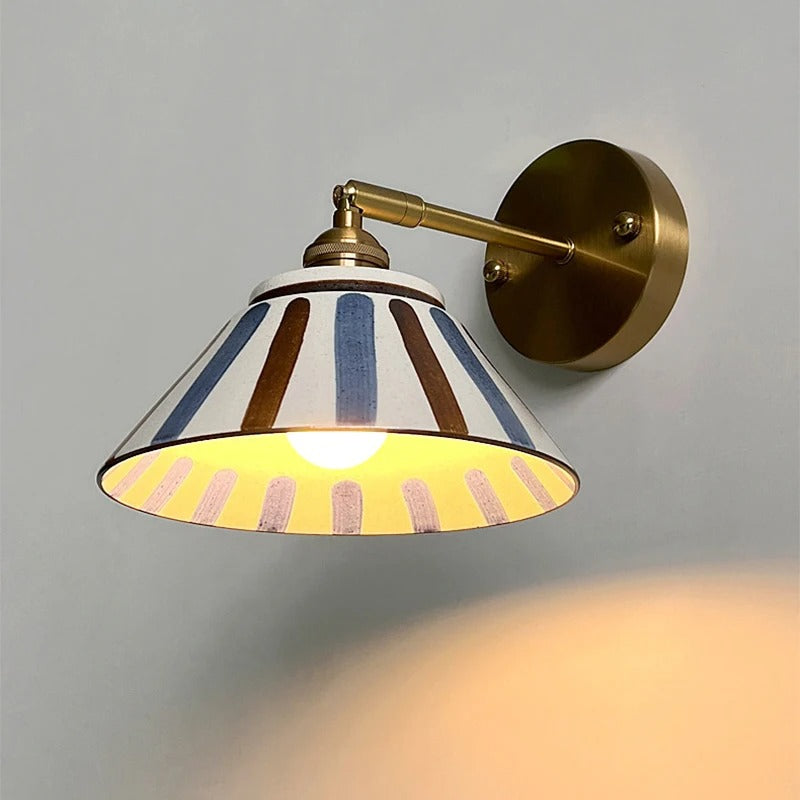 Brass wall sconce with ceramic shade in cream with blue and brown stripes, lit