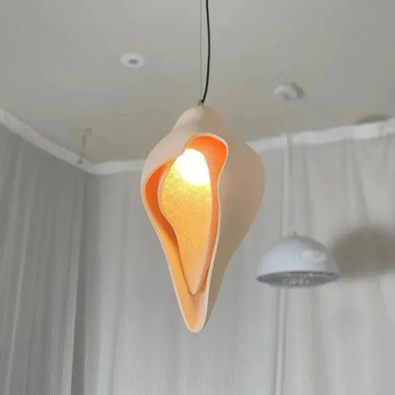 Conch shell pendant light in white with warm glowing gold interior, suspended from cord