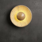 Single round backlit wall sconce with speckled tan travertine disc and dark insert