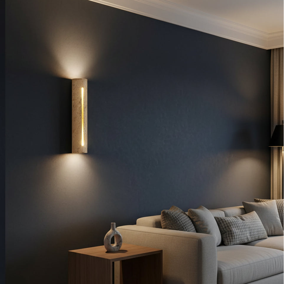 Beri travertine cylindrical vertical-slot wall sconce, lit warm on dark wall