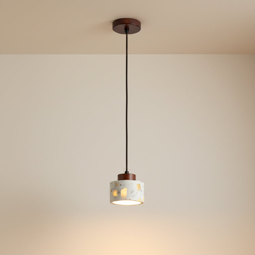 Cylindrical terrazzo pendant light with wood canopy and thin hanging cord, warm lit.