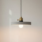 Concrete pendant light with wide round gray shade and brass socket, glowing bulb center