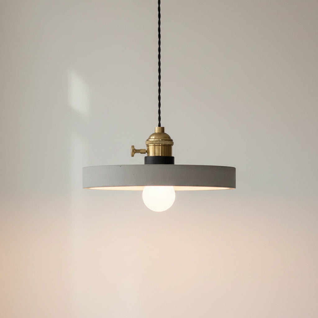 Concrete pendant light with wide round gray shade and brass socket, glowing bulb center