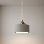 Concrete pendant light with round light-gray shade and brass socket, hanging from cord