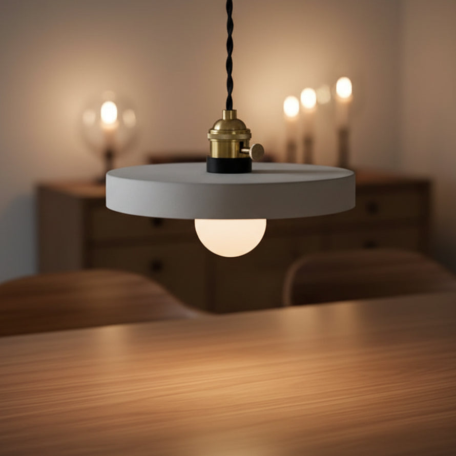 Concrete pendant light with round gray shade and brass socket, warm bulb glow