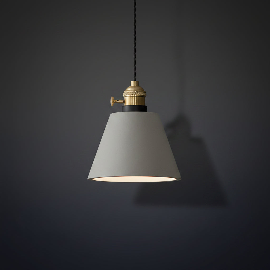 Concrete pendant light with light-gray cone shade and brass socket, hanging on black cord