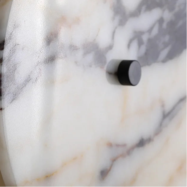 Wall sconce close-up: black cylindrical light housing in marble wall plate