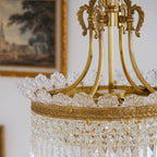 Gold canopy and curved arms above a clear crystal prism drum pendant light