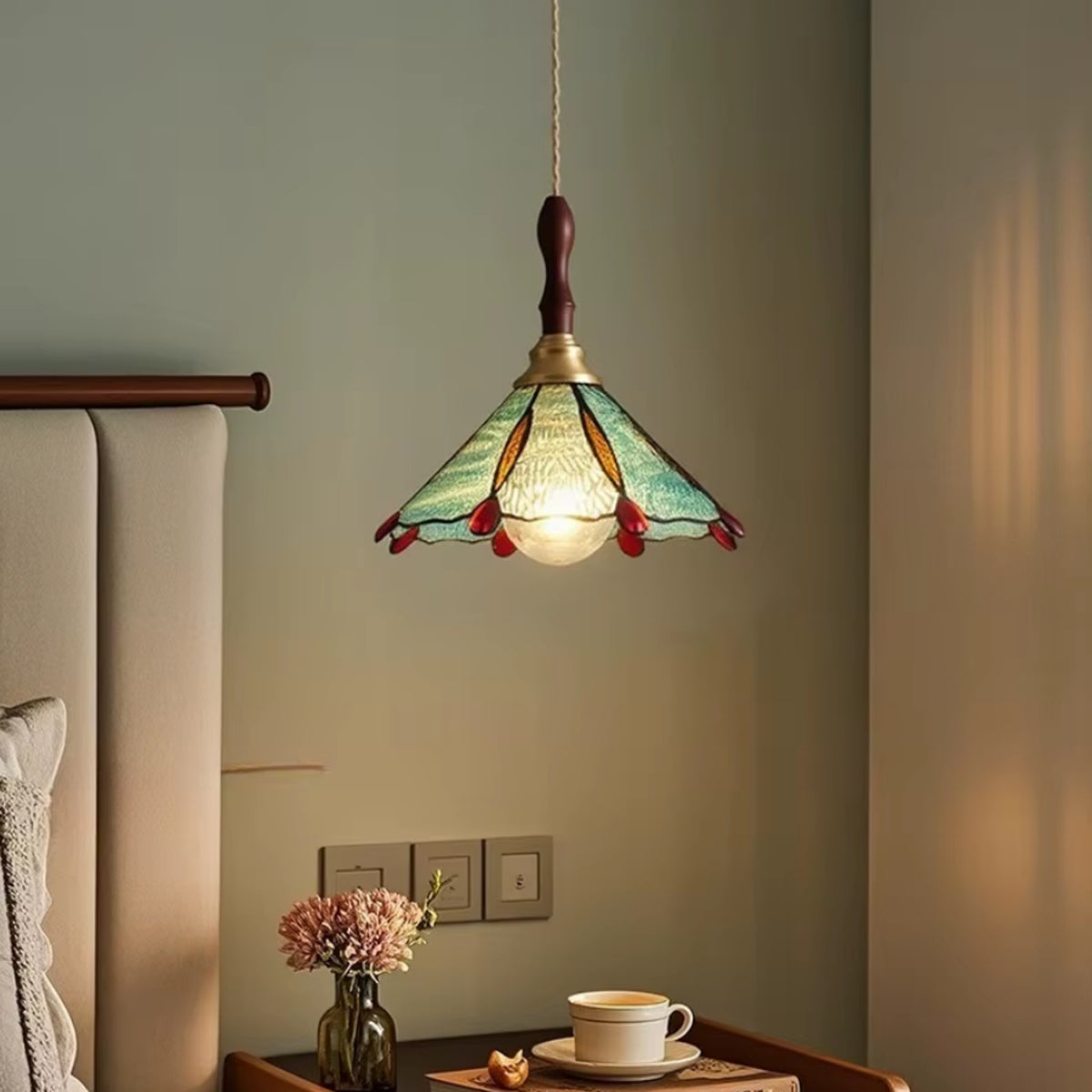 Scalloped stained-glass pendant light with green shade, brass cap, warm lit glow