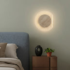 Round travertine backlit wall sconce with textured ring, warm glowing halo, and grey center