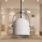 White speckled bell pendant light with black metal arch and warm gold interior.