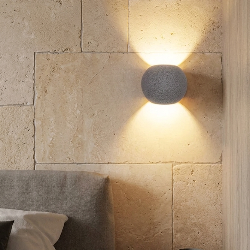Oval concrete wall light with textured globe shade, warm glow on stone wall