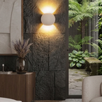 Oval concrete wall light with textured globe shade, warm light on dark stone wall