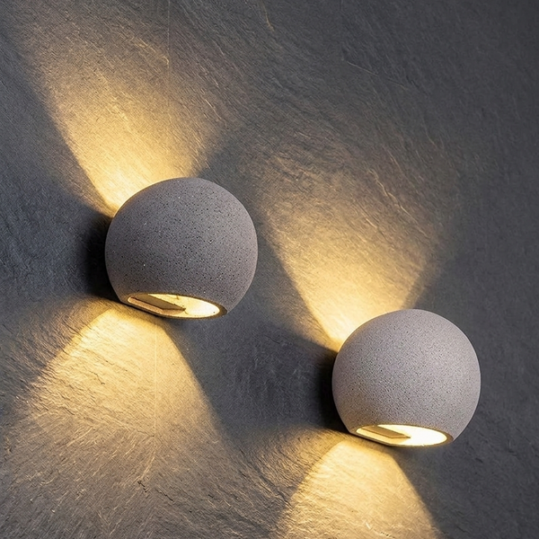 Pair of oval concrete wall lights with textured globe shades, warm beams on wall