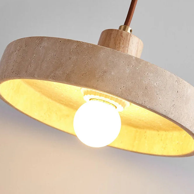Close-up of round travertine pendant shade glowing warm under a wood canopy