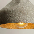 Speckled white concrete cylinder pendant light close-up with brass-toned interior